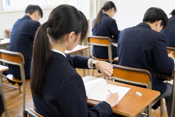 模試の本番で腕時計を見ながら時間配分を確認する制服姿の中学生