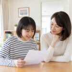 明るいリビングで、中学生の子どもと保護者が成績表を一緒に見ながら穏やかに話し合っている様子
