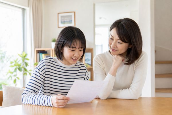 明るいリビングで、中学生の子どもと保護者が成績表を一緒に見ながら穏やかに話し合っている様子