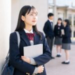 制服姿の女子高生が成績ファイルを胸に抱え、明るい高校の昇降口で前を見つめている