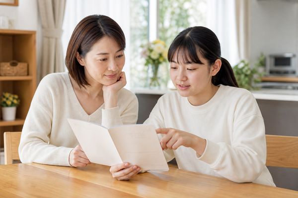 明るいダイニングテーブルで母親と中学生の娘が成績表を一緒に見ている様子