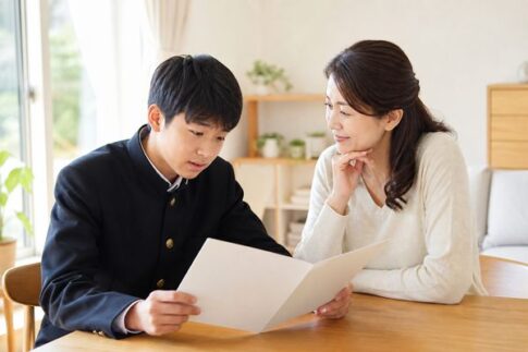 学生服の中学生と母親が明るいダイニングで通知表を開いて話している様子