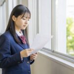 返却されたテストを校舎の窓際で静かに見つめる制服姿の高校生