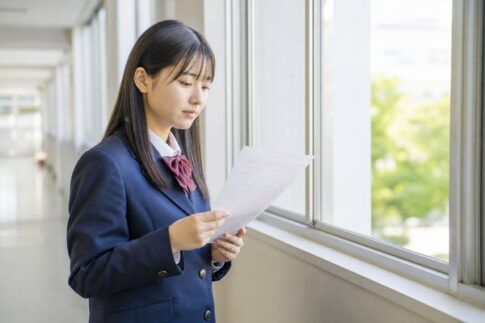 返却されたテストを校舎の窓際で静かに見つめる制服姿の高校生