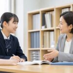 明るい高校の進路指導室で、制服姿の高校1年生が模試の準備について先生に相談している様子