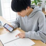 スマートフォンの勉強計画アプリと紙の予定表を見比べて1週間の勉強計画を立てている高校生