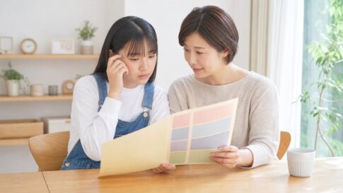 自宅で通知表を母親と一緒に見て考え込む中学生の女の子