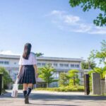 夏服の高校1年生が晴れた朝に校門から校舎へ向かって歩いている様子