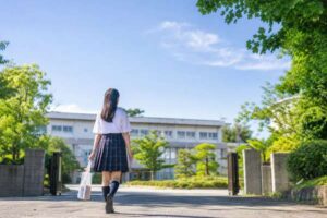 夏服の高校1年生が晴れた朝に校門から校舎へ向かって歩いている様子