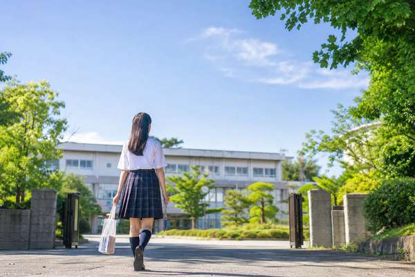 夏服の高校1年生が晴れた朝に校門から校舎へ向かって歩いている様子