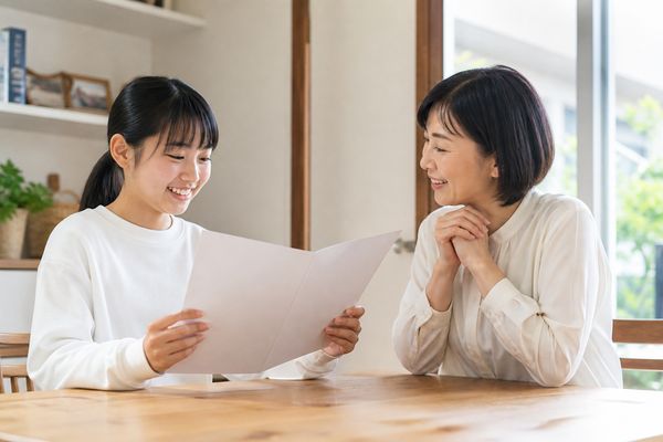 通知表を見て笑顔になる中学生と、隣で一緒に喜ぶ母親の様子