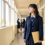 制服の高校生が明るい校舎の廊下で書類を手に、成績の基準を確かめようとしている様子