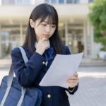 校門前で実力テストの結果を見ながら成績への影響を考えている中学生
