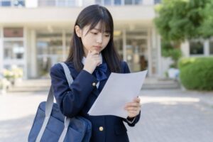 校門前で実力テストの結果を見ながら成績への影響を考えている中学生