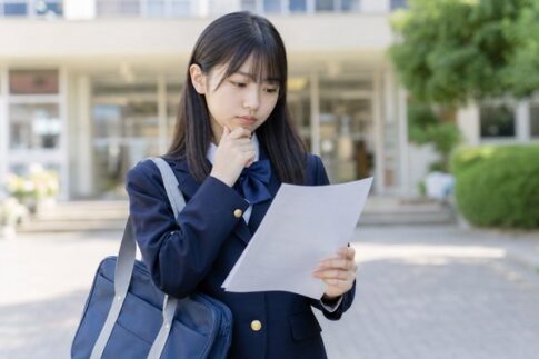 校門前で実力テストの結果を見ながら成績への影響を考えている中学生