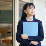 通知表のファイルを抱えて明るい廊下に立つ制服姿の中学生