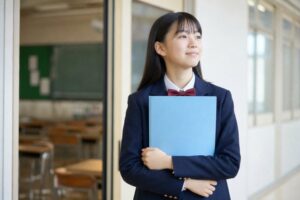 通知表のファイルを抱えて明るい廊下に立つ制服姿の中学生