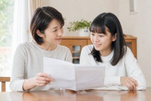 母親と中学生の娘が、明るいダイニングで通知表を広げて落ち着いて話し合っている様子