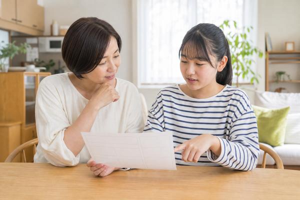 明るいダイニングで母親と中学生の娘が並んで座り、成績表を一緒に見ながら穏やかに話している様子