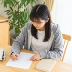 自宅の机で答案を見直しながらノートに書き込む女子学生