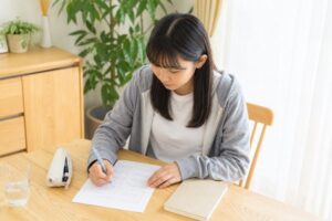 自宅の机で答案を見直しながらノートに書き込む女子学生