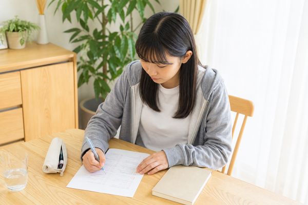 自宅の机で答案を見直しながらノートに書き込む女子学生