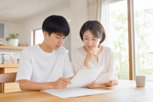 自宅のダイニングで中学生の息子と母親が通知表と資料を一緒に確認している様子