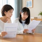 明るいダイニングテーブルで、私服の中学生と母親が学校の成績表と模試の棒グラフ入り結果シートを一枚ずつ手に持ち、並べて見比べている様子