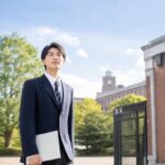 大学の正門前で、共通テストを終えた制服姿の高校生が成績表を手に前を見つめている様子