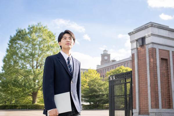 大学の正門前で、共通テストを終えた制服姿の高校生が成績表を手に前を見つめている様子