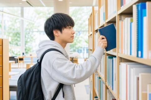 明るい図書館の書棚で、私服の高校生が自分のレベルに合う数学の問題集を1冊選び出している様子