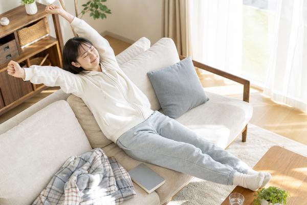 部屋着でソファに寝そべり、伸びをして休む高校生