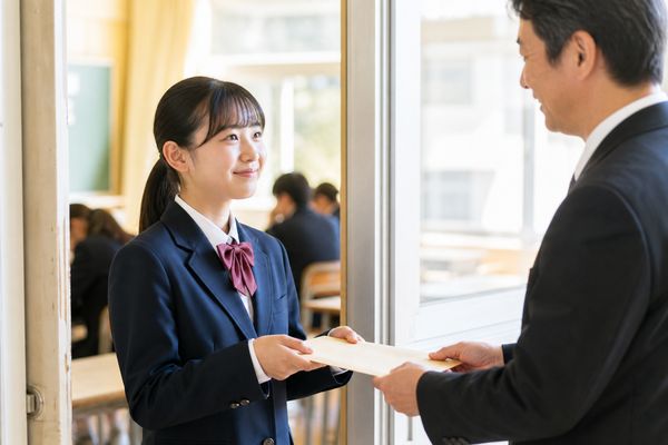教室の入口で先生から通知表の封筒を受け取り微笑む制服の中学生