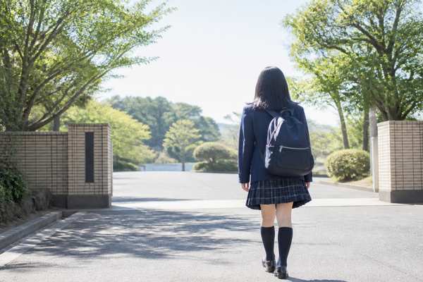 制服姿の中学生が朝の明るい校門へ向かって歩いていく後ろ姿