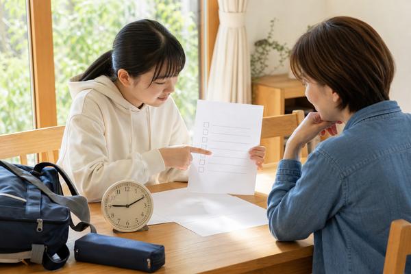 高校生と保護者がダイニングテーブルで受験の書類とチェックリストを一緒に確認している様子
