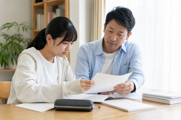 返却された模試の答案を父親と並んで静かに確認する私服の女子高校生