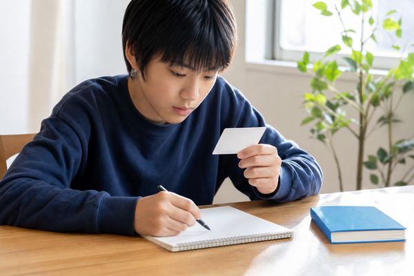 カードを見ながら思い出した内容をノートに書く男子中学生