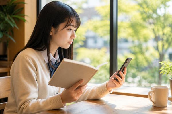カフェで単語帳とスマートフォンを見比べ、使う教材を選ぶ高校生