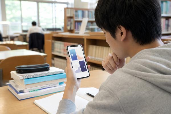 図書館の自習席でスマートフォンの勉強計画アプリを見比べている高校生