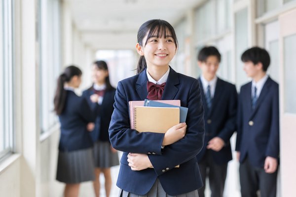 明るい校舎の廊下でノートを抱え自信を持って微笑む制服の女子中学生