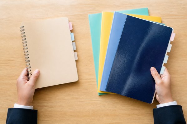 一冊の数学ノートと、複数教科の課題を重ねたノートを、机の上で左右に分けている中学生の手元