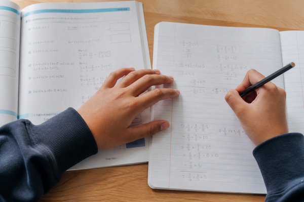 中学生が数学の基本問題をノートに解き直し、教科書と見比べながら手を動かしている手元