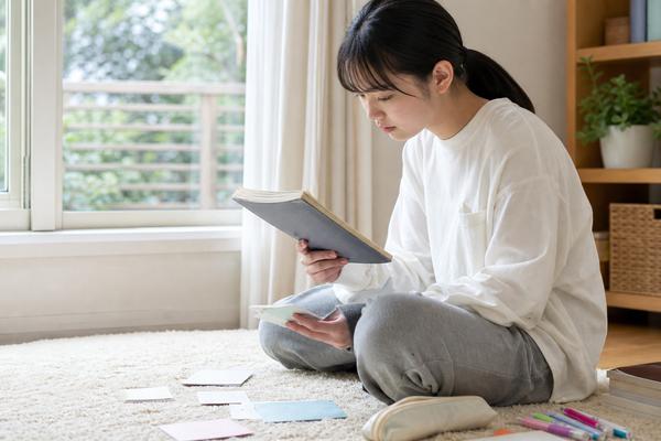 高校生が窓辺の床で使い慣れたノートと単語カードだけを短く見直している様子