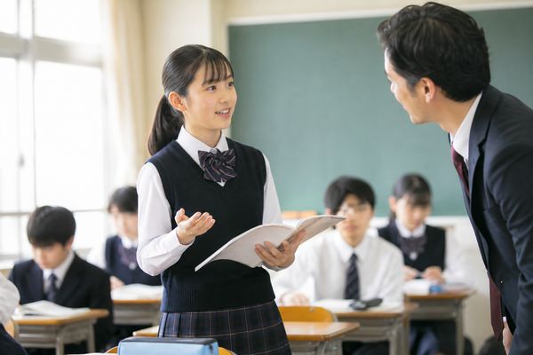 教室で中学生が手を挙げて自分の考えを先生に説明している場面