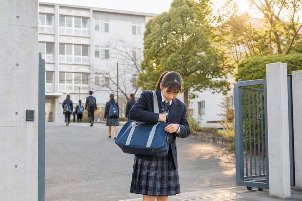 部活帰りの中学1年生が校門でかばんの中身を確かめ、翌日の準備を確認している様子