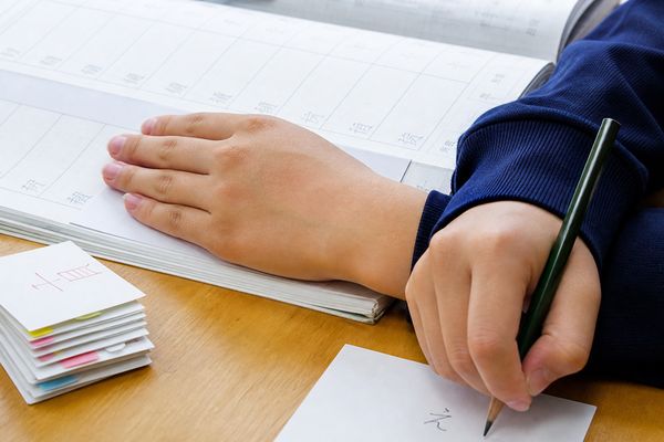 漢字ドリルの答えを手で隠して別の紙に書き取り練習をする中学生の手元