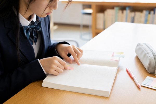 制服の高校生が学校の教材に付箋を貼りながら模試前の見直し範囲を絞っている様子