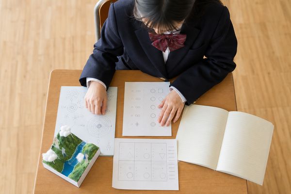 中学生が教室の机の上に、ワーク・作品・小テスト・振り返りノートなど評価の材料になる学習物を並べている俯瞰の様子
