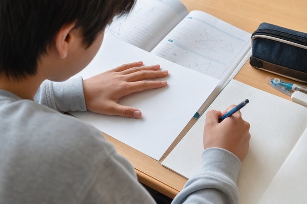 答えのページを手で隠し、何も見ずにもう一度問題を解き直している中学生