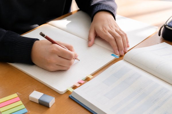 明るい机の上で、色付きの付せんを貼ったノートに鉛筆で間違い直しをする高校生の手元